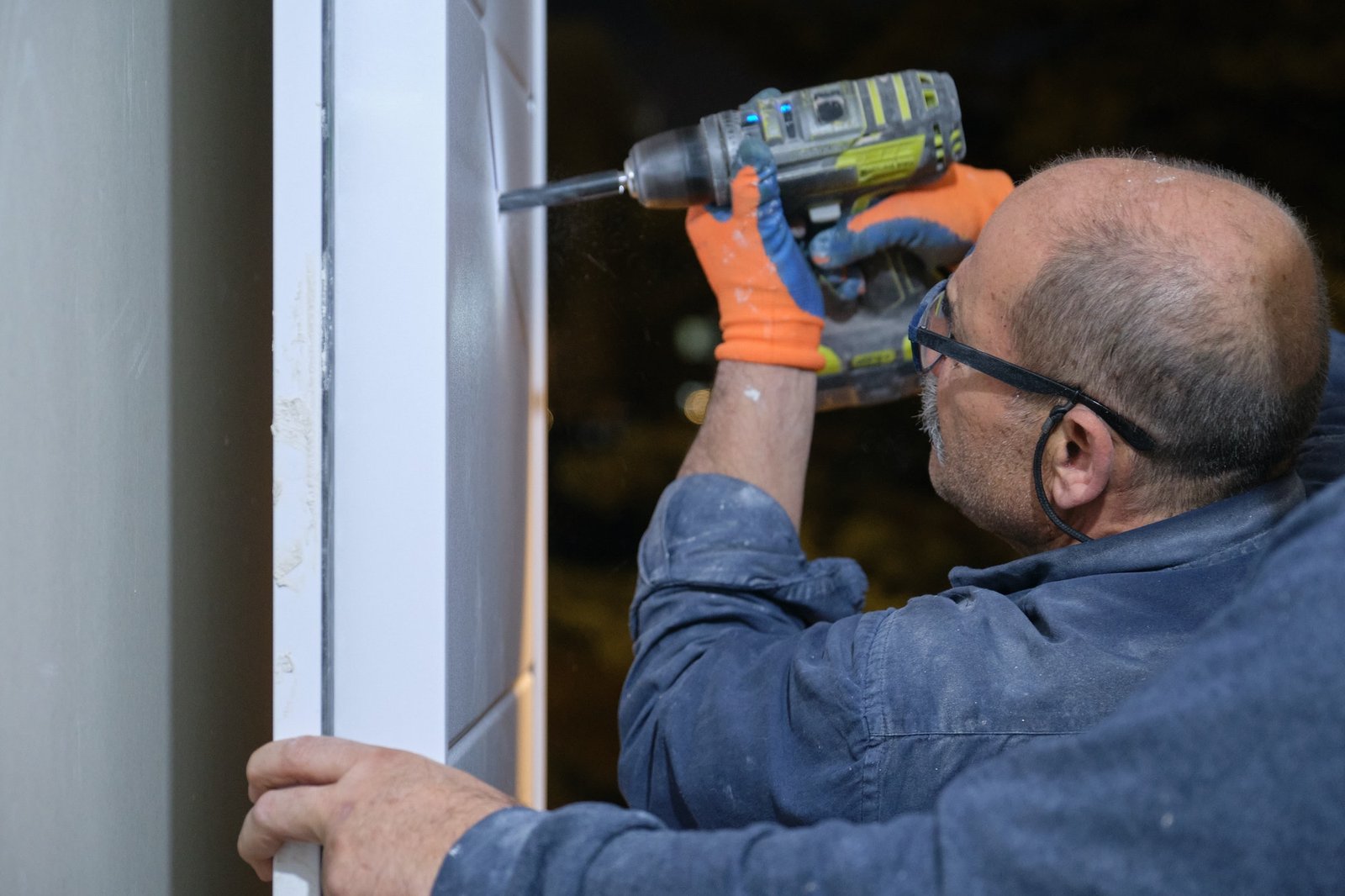 Senior worker installing a peephole in a new door using a drill.